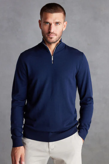 Man wearing a navy blue zip-up sweater posing for a photo against a gray background